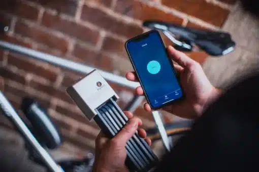Lülilukk Squire Inigma FL1 Bluetoothiga | E-pood Tootemaailm Käes hoitav nutitelefon ja hall juhtmevaba elektroonikaseade jalgratta kõrval