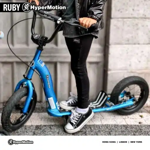 Laste tõukeratas HyperMotion RUBY 12.2 käsipiduritega | E-pood Tootemaailm Laps seisab sinisel HyperMotion tõukerattal, mustade rehvide ja juhtrauaga.