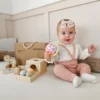 Montessori mänguasjakomplekt beebidele 7–12 kuud, 6-osaline | E-pood Tootemaailm Beebi istub mänguasjade keskel ja hoiab värvilist palli, taustal puidust mänguasjad ning Mamabrumi karp