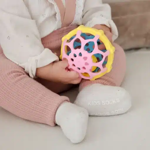 Montessori mänguasjakomplekt beebidele 7–12 kuud, 6-osaline | E-pood Tootemaailm Beebi hoiab käes värvilist roosakollast mängupalli, seljas valge pluus ja roosad püksid