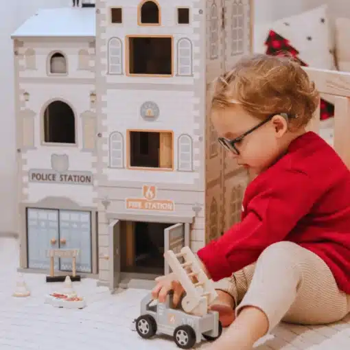 Puidust tuletõrje- ja politseijaama mängukomplekt lastele | E-pood Tootemaailm Laps mängib mängulinna ees tuletõrjeauto mänguasjaga
