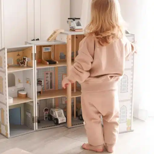 Puidust tuletõrje- ja politseijaama mängukomplekt lastele | E-pood Tootemaailm Laps beežis dressikomplektis mängib puidust mängumaja ja nukumööbli juures