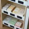Laste puidust mängupood kassaga 3+ | E-pood Tootemaailm Valge sahtlitega hoiukapp, milles on eri värvi karbid ja pakendid