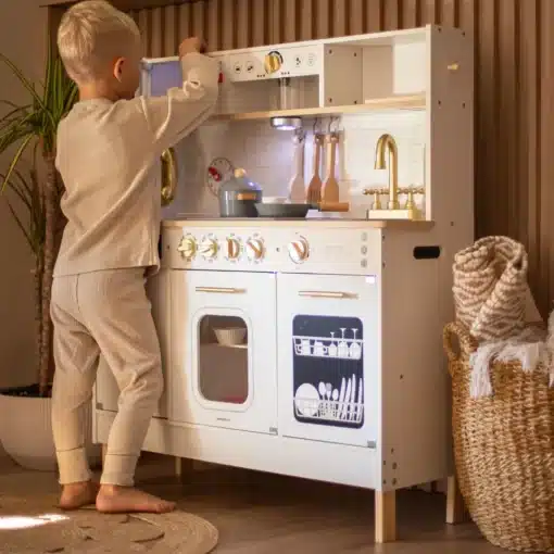 Interaktiivne XXL puidust mänguköök LED-valgustuse ja tarvikutega | E-pood Tootemaailm Laps mängimas valge mänguköögiga, millel on pliit, kraanikauss, ahi ja nõudepesumasin