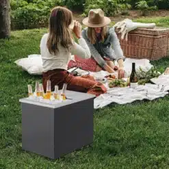 Must ristkülikukujuline joogijahuti murul pikniku kõrval, taustal kaks naist tekil.