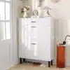 Kitsas jalanõudekapp 3 tasapinna, sahtli ja klappustega | E-pood Tootemaailm Valge kingakapp kolme sahtliga ja mustade jalgadega esikus, all sussid ja kõrval vihmavarjuhoidja.