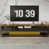 Kõrgläikega telerikapp 3 sahtli ja LED-valgustusega | E-pood Tootemaailm Moodne must ja kuldne TV-alus ning seinal riputatud digitaalne kell elutoas