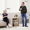 Kitsas sahtli ja riiulitega abilauake diivani kõrvale | E-pood Tootemaailm Pruunist ja mustast materjalist väike riiul diivani kõrval elutoas, mõõtmed 58,5 cm kõrgusega, kõrval istuv naine ja seisev mees võrdluseks
