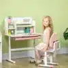 Reguleeritava kõrgusega laste kirjutuslaud ja tool riiuliga | E-pood Tootemaailm Laps istub roosa-valge reguleeritava õppelaua ja tooli komplekti ees toas