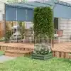 Puidust terrassil sinise varikatusega istumisala ja rohelise ronitaime tugiraam lillekastis