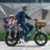 Elektriline kargoratas FIIDO T2 Longtail Cargo, Forest Green | E-pood Tootemaailm Mees sõidab elektrirattaga, ees korv ja taga kaks last turvakiivritega