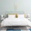 Seinale kinnitatav öökapp sahtli ja avatud riiuliga 2 tk | E-pood Tootemaailm Helerohelise metallraamiga voodi valge tekikoti, valgete patjade ja kollaste dekoratiivpatjadega