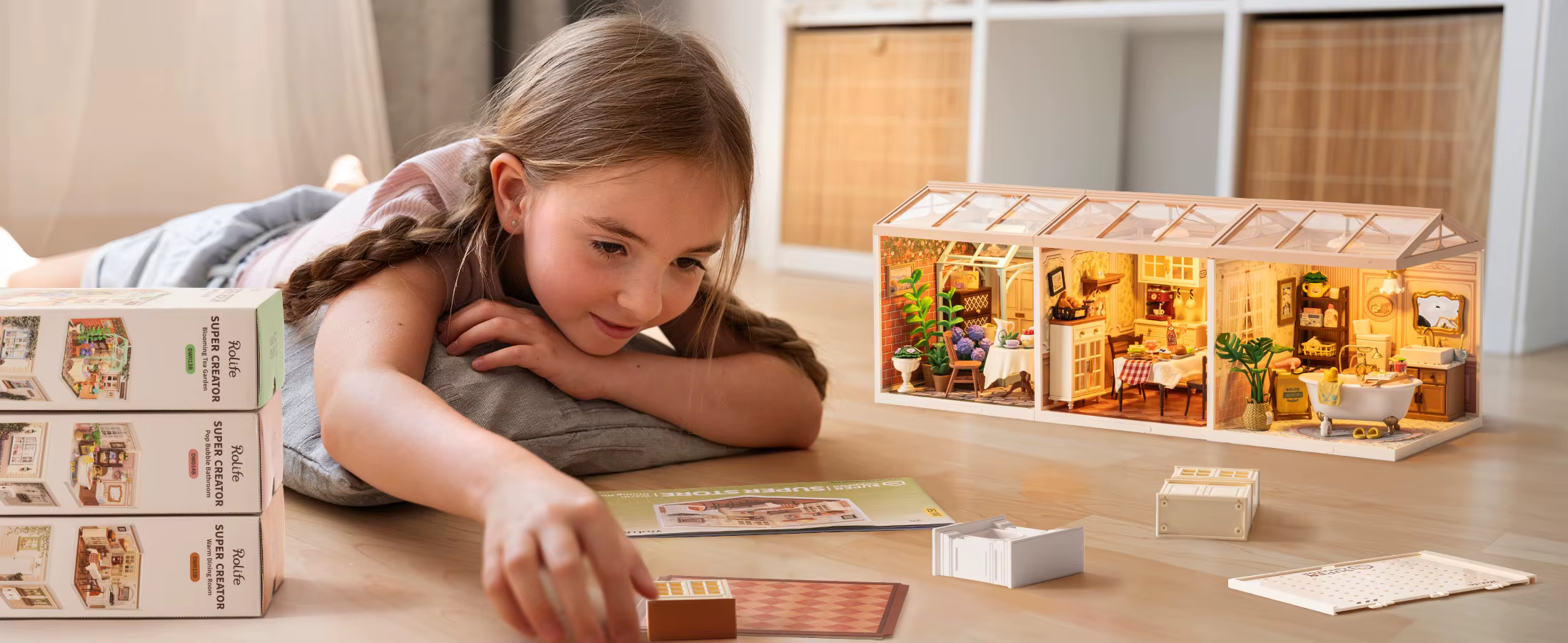 Tüdruk valgustatud miniatuurse majamudeli kõrval, laual mudelikomplekti karbid ja detailid.