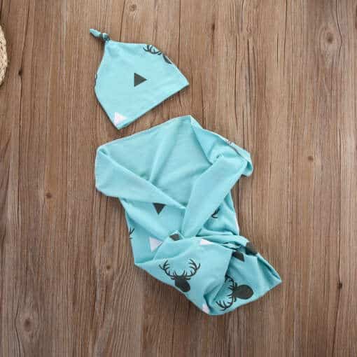 sinine puuvillast beebitekk ja müts puidust pinnal, kaunistatud hirve ja kolmnurkade mustriga