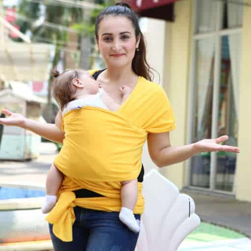 naine kannab kollast beebi kandmise lina, milles magab beebi