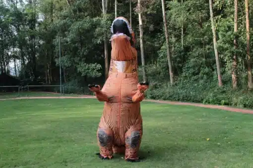 täiskasvanu kannab täispuhutavat T-Rex kostüümi rohelisel murul