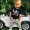 väike laps mustas t-särgis ja hallides pükstes seisab valge mänguauto kõrval