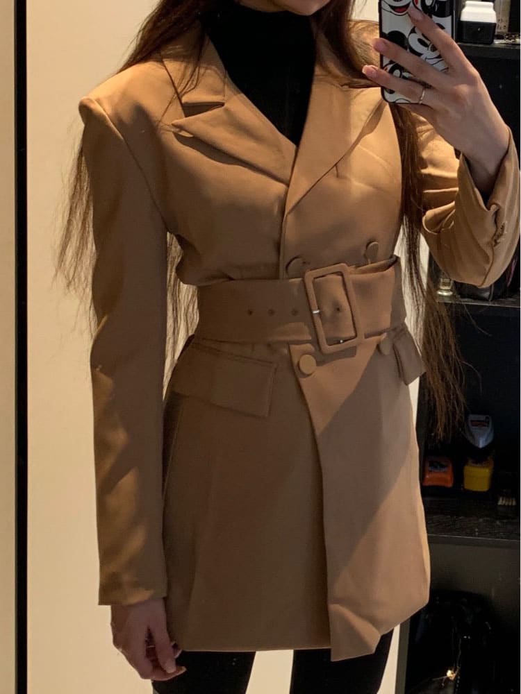Elegantne khaki mantel ripub puidust riidepuul helehalli taustaga.