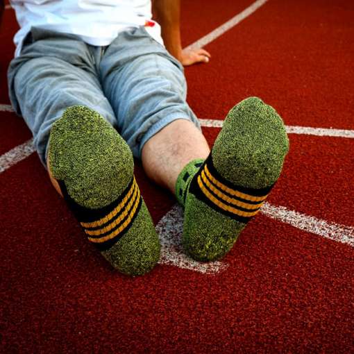 mees istub spordiväljakul, jalas rohelised sokid musta ja kollase triibuga