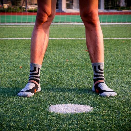 mees seisab jalgpalliväljakul hallide ja mustade mustriliste spordisokkidega