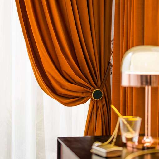 oranžid sametist kardinad, mis on seotud küljele, kõrval on lamp ja laud
