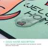 roheline uksematt, millel on armas illustratsioon ja tekst 'welcome home', vesi voolab mati peale