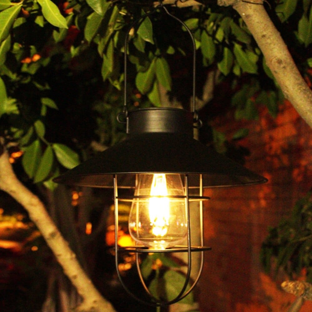 must metallist vintage stiilis latern, mis ripub puuoksal ja valgustab aeda sooja valgusega