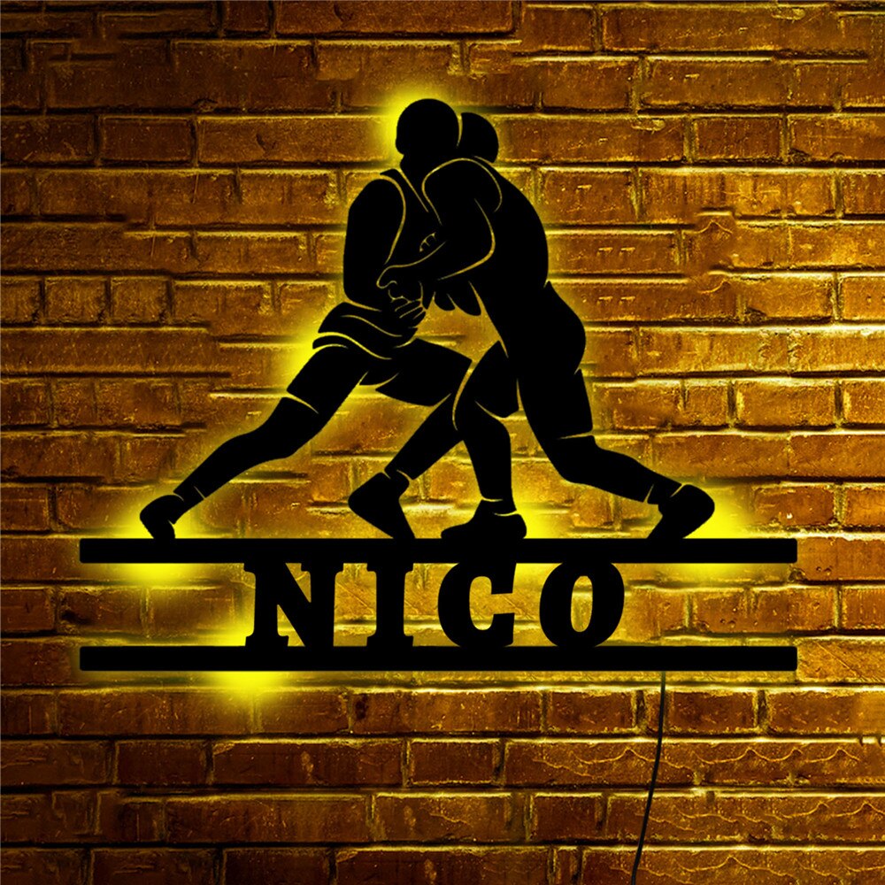 kaks maadlejat siluetina telliskiviseinal, mille all on nimi 'Nico' ja kollane LED-valgustus