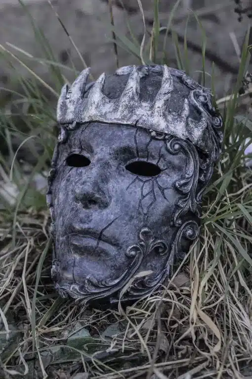 tume hall mask, millel on krooni kujundus ja keerulised mustrid, asetatud rohu sisse